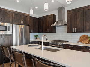 Kitchen with a sink, high quality appliances, hanging light fixtures, light stone countertops, and wall chimney exhaust hood