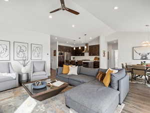 Living area with light wood finished floors, ceiling fan with notable chandelier, vaulted ceiling, and recessed lighting