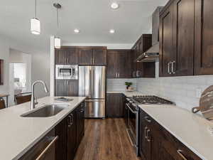 Kitchen featuring premium appliances, a sink, dark wood-style floors, wall chimney exhaust hood, and decorative light fixtures