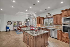 Kitchen featuring light stone counters, brown cabinets, stainless steel appliances, backsplash, and a sink