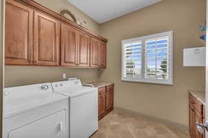 Clothes washing area with washing machine and dryer, cabinet space, baseboards, and light tile patterned flooring