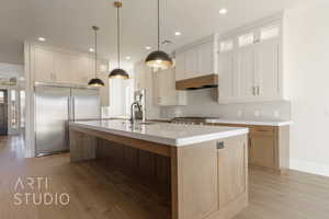 Kitchen featuring built in appliances, light wood-style flooring, visible vents, light countertops, and an island with sink