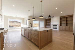 Kitchen with a sink, light countertops, light wood finished floors, a glass covered fireplace, and a center island with sink