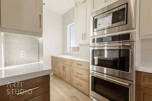 Kitchen with stainless steel appliances, light wood-type flooring, light countertops, and decorative backsplash