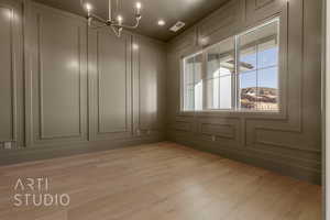 Empty room featuring light wood finished floors, visible vents, and a decorative wall