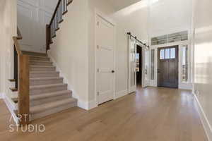 Entrance foyer with stairs, light wood-style flooring, baseboards, and a barn door