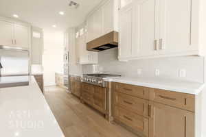 Kitchen with light wood finished floors, visible vents, wall chimney exhaust hood, built in appliances, and light countertops