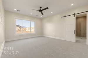 Unfurnished bedroom featuring ceiling fan, a barn door, recessed lighting, light colored carpet, and baseboards