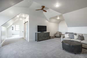 Living room featuring carpet floors, lofted ceiling, a ceiling fan, and a barn door