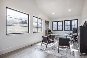 Office area featuring a wealth of natural light, vaulted ceiling, baseboards, and wood finished floors