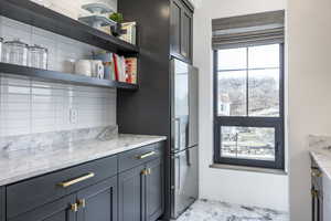 Kitchen featuring light stone counters, freestanding refrigerator, marble finish floor, and open shelves