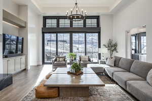 Living room with a towering ceiling, a chandelier, a raised ceiling, and wood finished floors