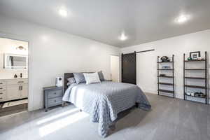 Carpeted bedroom with a barn door, baseboards, and connected bathroom