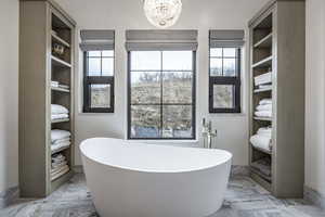 Full bath featuring a freestanding bath, marble finish floor, and a notable chandelier