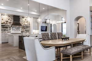 Dining room with light wood-type flooring, arched walkways, and recessed lighting