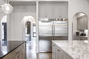 Kitchen with wood finished floors, gray cabinets, light stone countertops, and stainless steel built in fridge