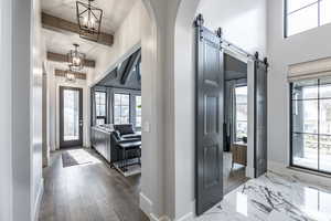 Entryway with arched walkways, a barn door, wood finished floors, baseboards, and an inviting chandelier