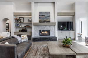 Living area with arched walkways, wood finished floors, a high end fireplace, and built in features