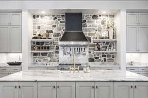 Kitchen with range, custom exhaust hood, decorative backsplash, and light stone counters