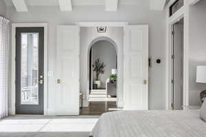 Bedroom featuring access to exterior, arched walkways, beam ceiling, and wood finished floors