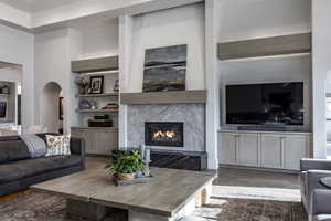 Living room featuring built in features, arched walkways, wood finished floors, and a premium fireplace