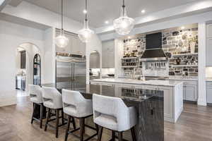 Kitchen featuring arched walkways, a center island, stainless steel built in fridge, and wall chimney range hood