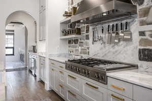 Kitchen featuring dark wood-style flooring, open shelves, tasteful backsplash, stainless steel gas stovetop, and ventilation hood