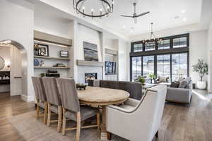 Dining room featuring arched walkways, a glass covered fireplace, wood finished floors, and a towering ceiling