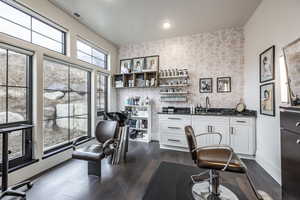 Home office featuring dark wood-style flooring, indoor wet bar, a sink, baseboards, and wallpapered walls