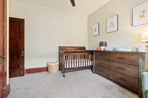 Carpeted bedroom featuring a crib, baseboards, and a ceiling fan