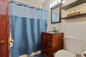 Bathroom with a shower with curtain, wainscoting, vanity, and toilet