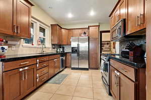 Kitchen featuring stainless steel appliances, dark stone counters, a sink, and light tile patterned floors