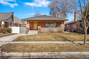 Bungalow-style home with a front lawn, fence, a porch, and brick siding