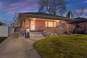 View of front of house featuring an outbuilding, brick siding, a yard, covered porch, and fence