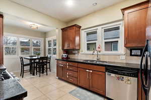 Kitchen with light tile patterned flooring, a sink, black fridge with ice dispenser, brown cabinets, and dishwasher