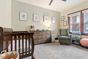 Carpeted bedroom with ceiling fan, a crib, and baseboards