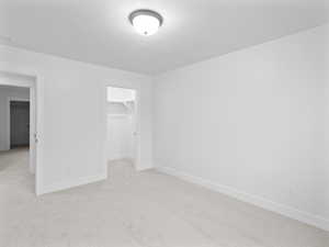 Unfurnished bedroom with light carpet, baseboards, a closet, and a walk in closet