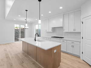 Kitchen with premium range hood, white cabinets, light wood finished floors, and a sink