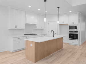 Kitchen featuring light wood finished floors, light countertops, custom range hood, white cabinets, and appliances with stainless steel finishes
