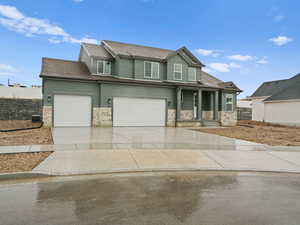 View of front of property featuring an attached garage, driveway, stone siding, and a shingled roof