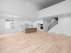 Unfurnished living room with visible vents, light wood-style floors, and a notable chandelier