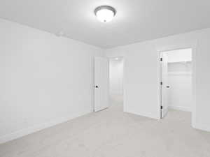 Unfurnished bedroom with light carpet, a textured ceiling, baseboards, a spacious closet, and a closet