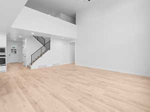 Unfurnished living room with stairway, visible vents, light wood finished floors, and baseboards