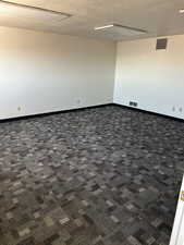 Empty room with dark colored carpet, visible vents, a textured ceiling, and baseboards