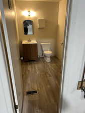 Half bathroom featuring toilet, wood finished floors, vanity, visible vents, and baseboards