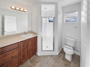 Full bathroom featuring toilet, vanity, baseboards, a shower stall, and stone finish floor