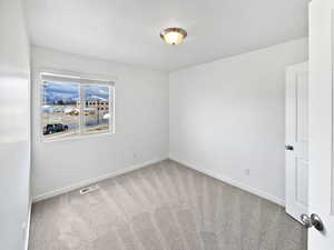 Carpeted spare room with a textured ceiling, visible vents, and baseboards