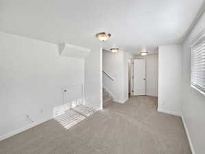 Spare room with light carpet, stairs, baseboards, and a textured ceiling