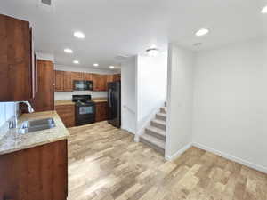 Kitchen featuring a sink, visible vents, light wood-style floors, light stone countertops, and black appliances