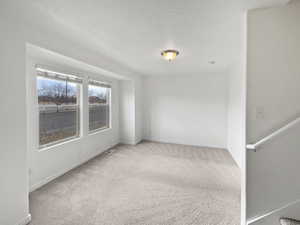 Spare room featuring carpet flooring, a textured ceiling, and baseboards